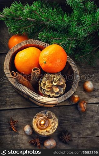 Still-life with candle and tangerines. Wooden bucket with tangerines and pine cones on the background of Christmas trees