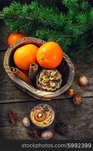 Still-life with candle and tangerines. Wooden bucket with tangerines and pine cones on the background of Christmas trees