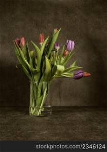 Still life with colorful tulips in vase of glass with brown background