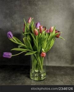 Still life with colorful tulips in vase of glass with brown background. vase of glass with stil life of tulips
