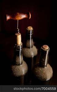 Still-life with dusty vintage wine bottles and old wooden corkscrew over black background