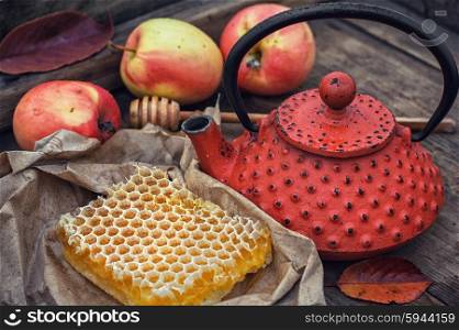Still life with honeycombs. Honeycomb wrapped in grey paper on the background of the red kettle