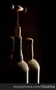 Still-life with old dusty wine bottles and corkscrew over black background