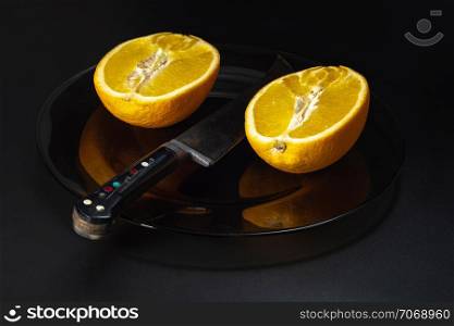 Still life with orange oranges and a large knife on a dark plate and a black background.