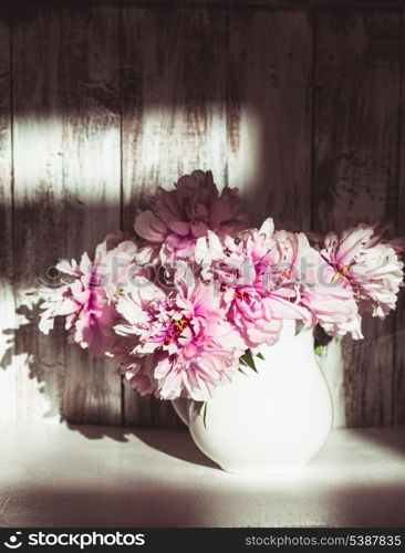 Still life with peonies over shabby wooden wall with sunlight from window