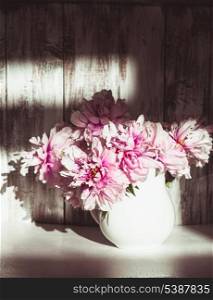 Still life with peonies over shabby wooden wall with sunlight from window