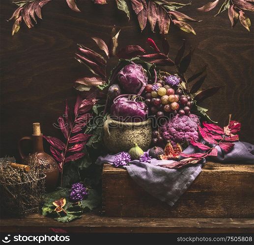 Still life with purple fruits and vegetables on wooden table with autumn leaves. Copy space for your design