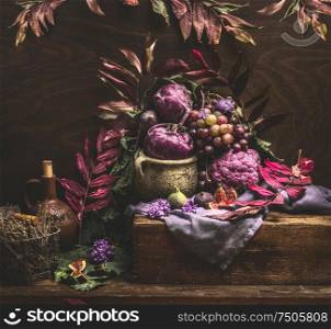 Still life with purple fruits and vegetables on wooden table with autumn leaves. Copy space for your design