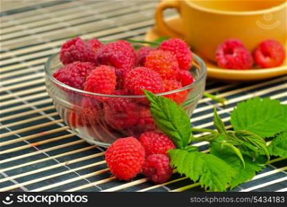 Still life with raspberries and green leafs on striped placemat, close up