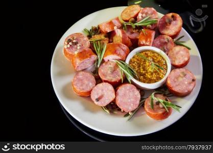 still life with sliced sausage, pepper, rosemary, mustard. on black background