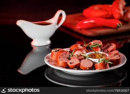 still life with sliced sausage, pepper, rosemary, sauce and mustard. on black background