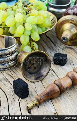 Still life with smoking hookah and grapes on wooden background. Smoking hookah is in the details