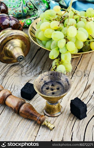 Still life with smoking hookah and grapes on wooden background. Smoking hookah is in the details