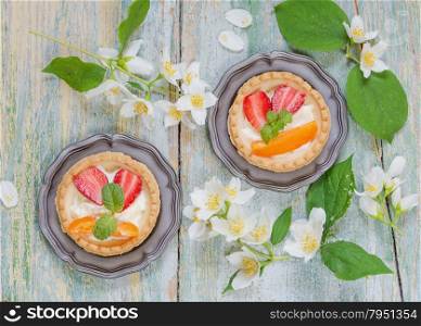Still-life with tartlets filled with cream and berries and jasmine flowers on old shabby boards, top view