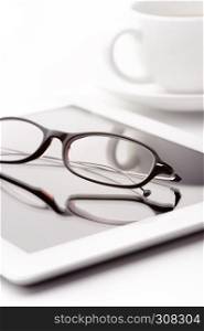Still life with white tablet, coffee cup and glasses on a white table. White tablet, coffee cup and glasses on a white table