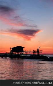 Stilt house in silhouette over the sea during a beautiful red sunset. Stilt house in silhouette over the sea