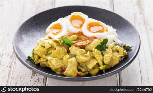Stir Fried Chicken with Green Curry Paste, Steamed Rice and Runny Yolk Boiled Egg in black ceramic plate on white old wood texture background, Pud Keow Wan Gai, Thai food