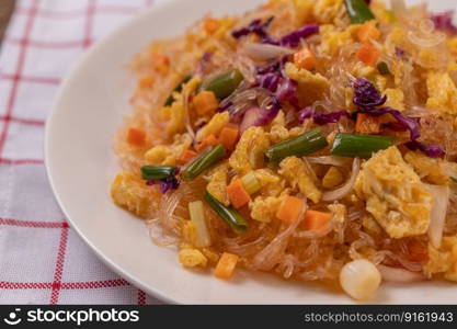 Stir fried glass noodles with eggs and put on a plate on a red white cloth.