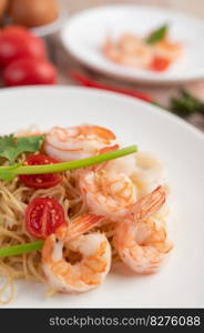 Stir-fried instant noodle with prawn and crab stick along with tomatoes and peppers in a white plate on a wooden floor.