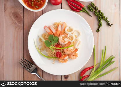 Stir-fried instant noodle with prawn and crab stick along with tomatoes and peppers in a white plate on a wooden floor.