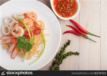 Stir-fried instant noodle with prawn and crab stick along with tomatoes and peppers in a white plate on a wooden floor.
