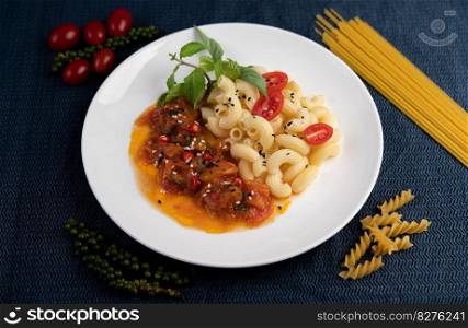 Stir-fried macaroni with tomato, chili, pepper seeds and basil in a white dish.