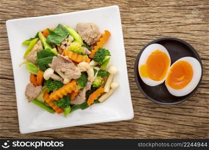 stir fried mixed vegetables with pork and shimeji mushroom beside boiled egg in ceramic plate on rustic natural wood texture background, top view