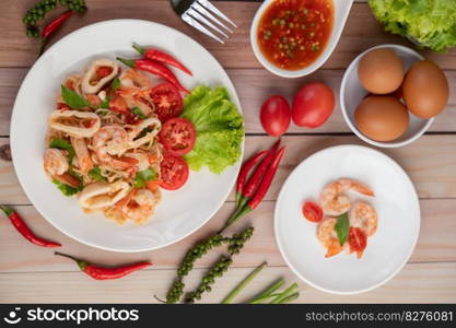 Stir-fried noodles with squid, tomatoes, peppers, chives, Celery and crab sticks in a white plate on a wooden floor.