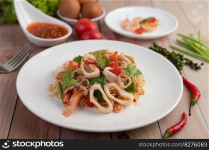 Stir-fried noodles with squid, tomatoes, peppers, chives, Celery and crab sticks in a white plate on a wooden floor.