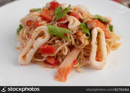 Stir-fried noodles with squid, tomatoes, peppers, chives, Celery and crab sticks in a white plate on a wooden floor.