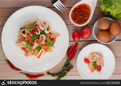 Stir-fried noodles with squid, tomatoes, peppers, chives, Celery and crab sticks in a white plate on a wooden floor.