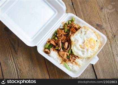 Stir fried pork with red curry paste and basil leaves with yardlong bean and fried egg topped in a plastic box, Thai street food or food delivery
