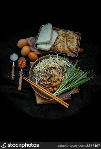 Stir fried soft turnip cake or Fried radish cake (chai tow kway) with bean sprout and chives in ceramic plate served with suger, ground dried chili. Thai - Chinese food called Kanom Pak kad or Char Koay Kak, Top view, Copy space, Selective focus.