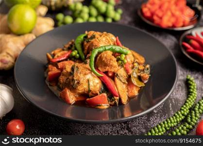 Stir-fried spicy Catfish in black plate with spices on black cement.