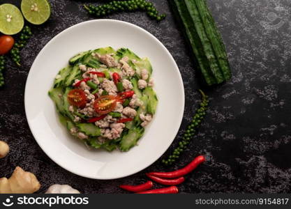 Stir fried zucchini with minced pork in white plate, and spices on a black cement floor