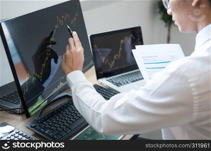Stock exchange trader Analyzing Graphs chart or data On Multiple Screens in office