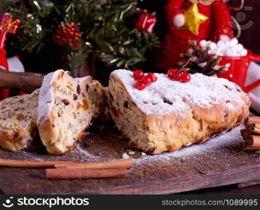 Stollen a traditional European cake with nuts and candied fruit, is dusted with icing sugar and cut into pieces on a brown wooden board