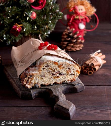 Stollen a traditional European cake with nuts and candied fruit, is dusted with icing sugar on a brown wooden board