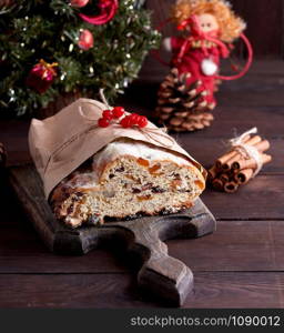 Stollen a traditional European cake with nuts and candied fruit, is dusted with icing sugar on a brown wooden board