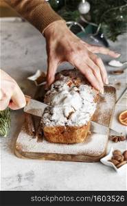 Stollen is fruit bread of nuts, spices, dried or candied fruit, coated with powdered sugar. Close up hands of the chef slicing a cake with a knife at pastry shop kitchen. Cooking Holiday Table