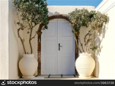 Stone arch, wooden door and a vase with a tree in front of her. Santorini. Oia.