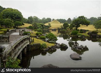 Stone bridge and gravel road along a lake in Suizenji garden, Kumamoto, Kyushu, Japan