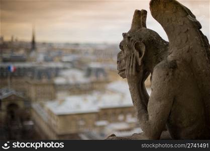 Stone gargoyle with horns, perched on a corner of the cathedral of Notre Dame, peering over the city of Paris.
