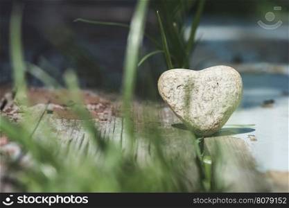 Stone heart shape on wood. Green grass
