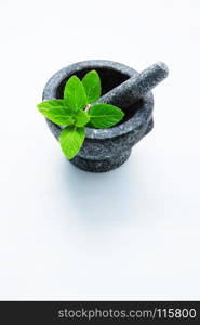 Stone mortar and pestle with peppermint leaf on white wooden background with copy space.