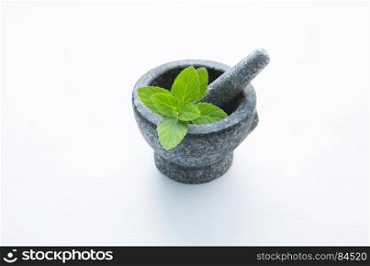 Stone mortar and pestle with peppermint leaf on white wooden background with copy space.
