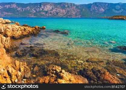 Stone seashore with turquoise clear water against the backround of mountains landscape. Summer background, travel concept. Landscape of blue clear sea water and stone cost