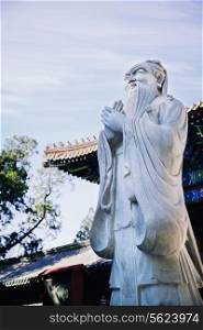 Stone statue of Confucius, traditional pagoda in the background