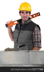 Stonemason standing before a wall and carrying a spirit level