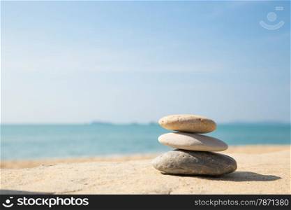 Stones balance, pebbles stack on the sand beach with shadow on right side , beautiful sea view during daytime on a sunny day with blue sky on background
